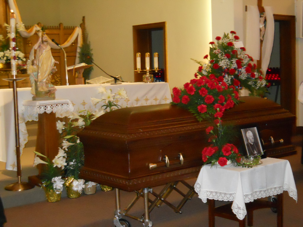 wooden casket with flower arrangement on top bishop rosmans funeral mass
